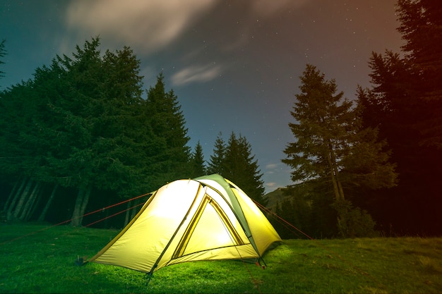 Туристическая палатка для туристов, ярко освещенная изнутри на зеленой травяной лесной поляне