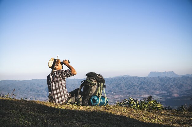 Tourist is watching through binoculars on sunny cloudy sky from mountain top.