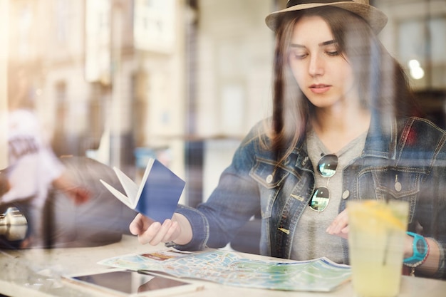 にぎやかな街でレモネードを飲んでパスポートを保持している地図を読んでカフェに座っている観光客