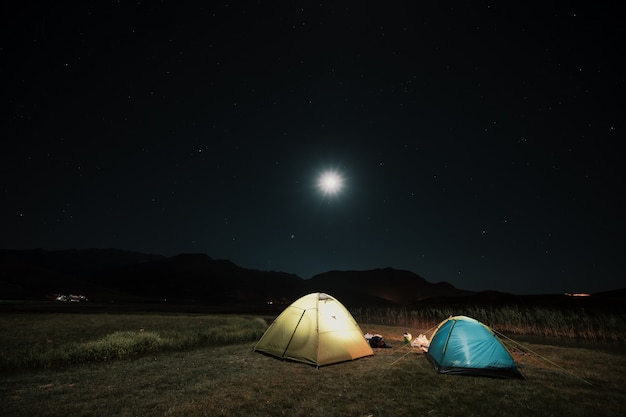 Tourist tents in camp among meadow in the night mountains