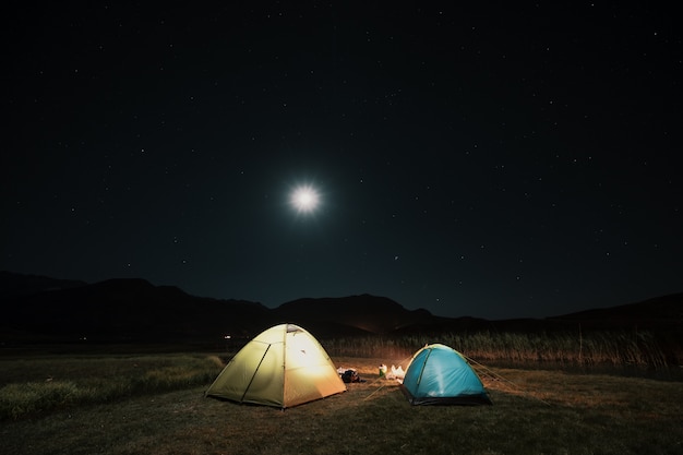 Tourist tents in camp among meadow in the night mountains