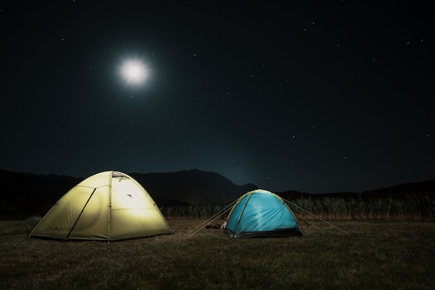 Tourist tents in camp among meadow in the night mountains