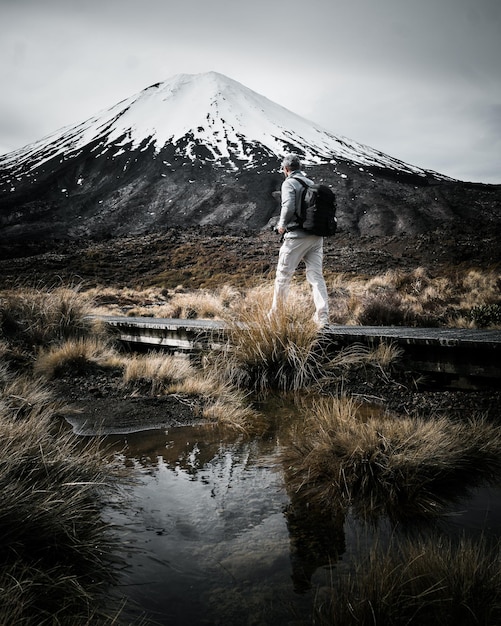 Tourist walking in the small footpath next to a bog with snow-capped mountain in the background