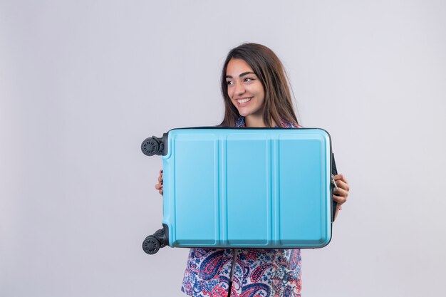 tourist woman holding travel suitcase looking aside smiling cheerfully, ready to holiday standing on isolated white