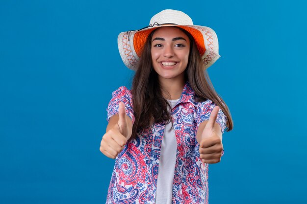파란색에 서 엄지 손가락을 보여주는 긍정적이고 행복 웃는 모자와 관광 여자
