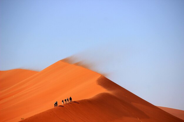 Tourists climbing up the sand dunes in the desert with the blue sky