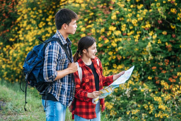 観光客の男性と女性は花畑の近くの地図を見ます。