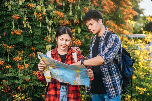 観光客の男性と女性は花畑の近くの地図を見ます。