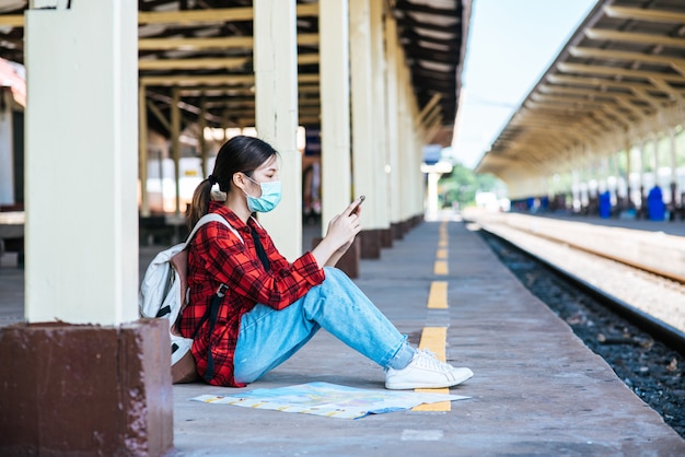 Tourists sitting and watching phones on the footpath beside the railway.