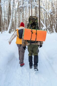Туристы с рюкзаками идут по зимней тропе в лесу, вид сзади
