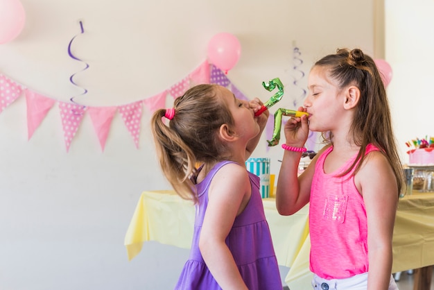 Free photo tow cute little girls blowing party horn