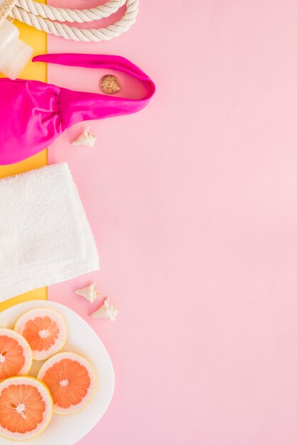 Towel near bottle with bag and swimsuit near fruits