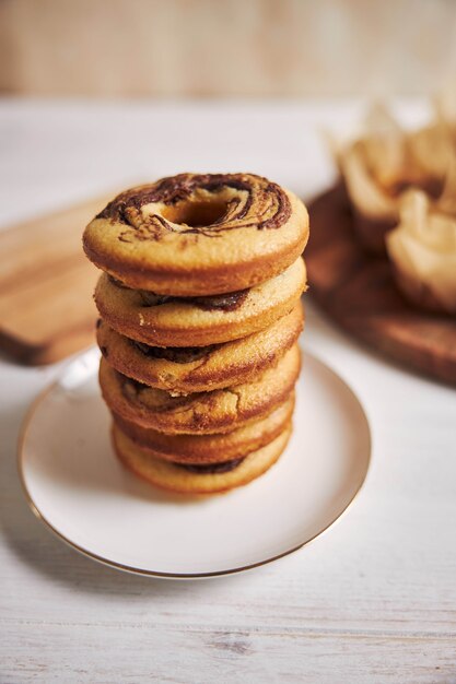 Tower of chocolate donuts on a plate near some chocolate muffins