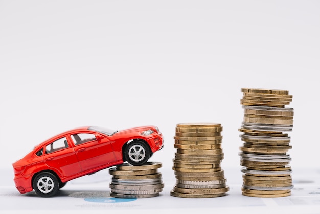 Toy car going up on the increasing stack of coins against white background