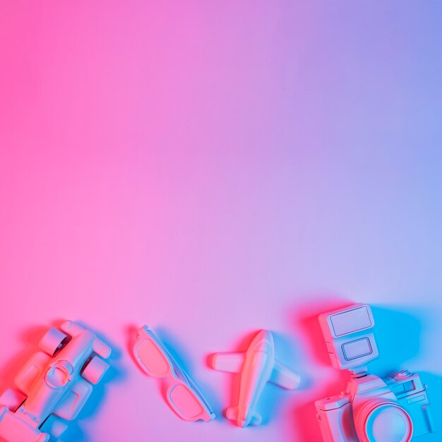 Toy car; plane; spectacle and camera arranged at the bottom of pink background with blue light