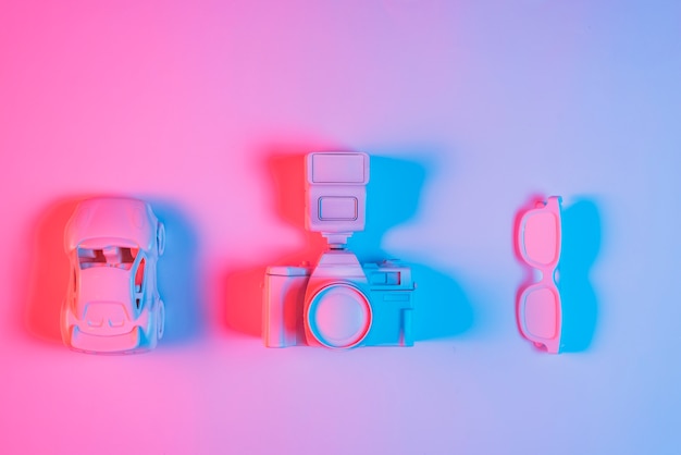 おもちゃの車;レトロなカメラと青い光の効果とピンクの背景に行に配置された眼鏡