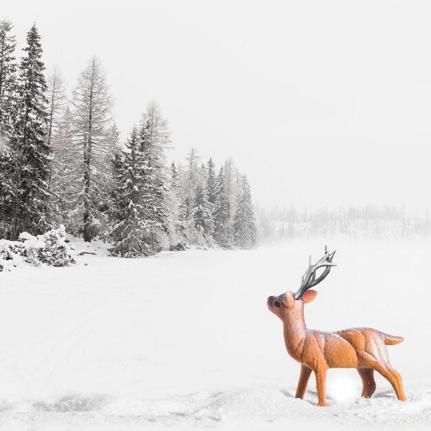 Игрушечный олень между полем с деревьями в снегу