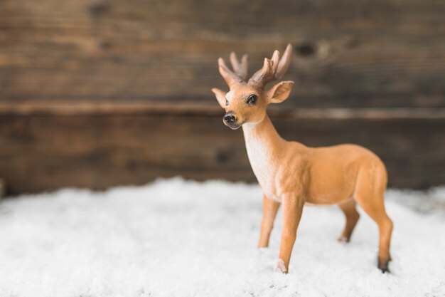 Toy deer on snow near wood wall