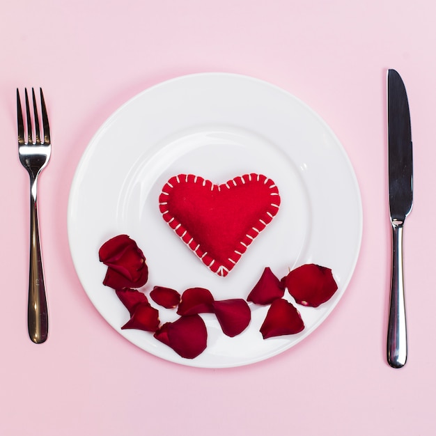 Toy heart with flowers petals on plate 