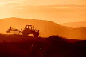 Free photo tractor in a farm field at sunset. backlight warm tones