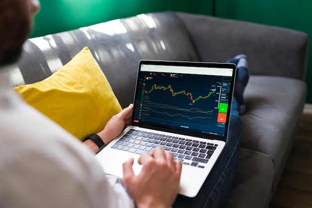 Trading finances. Young man resting on the couch while checking the stock market on the laptop