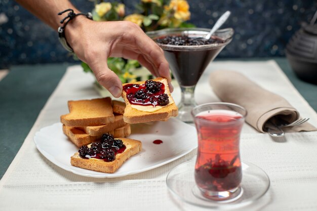 A traditional armudu glass of black tea with toasts with strawberry jam. A person taking a toast.