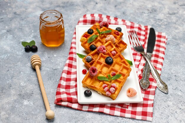 Traditional belgian waffles with fresh berries and honey on grey concrete surface. 