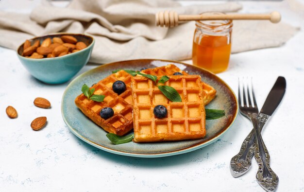 Traditional belgian waffles with fresh berries and honey on grey concrete surface. 