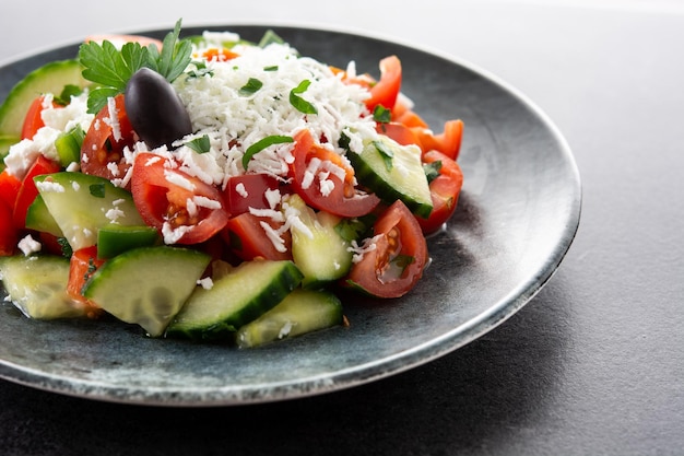 Traditional Bulgarian shopska salad with tomatocucumber and bulgarian sirene cheese on black background