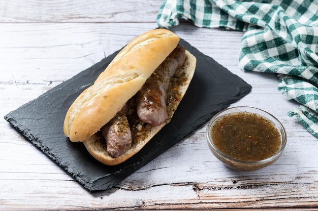 아르헨티나 의 전통적 인 choripan 샌드위치 는 나무 테이블 에 chorizo 와 chimichurri 소스 를 넣은 것 이다