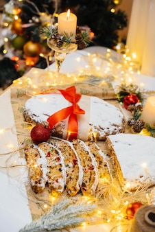 촛불이 있는 크리스마스 장식의 배경에 가루 설탕을 뿌린 말린 과일과 견과류로 만든 전통적인 크리스마스 스톨렌. 전통적인 크리스마스 컵 케 익입니다.