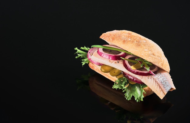 Traditional Dutch sandwich with herring and pickles cucumber and red onion on the dark mirror table. Close up, selective focus and copy space