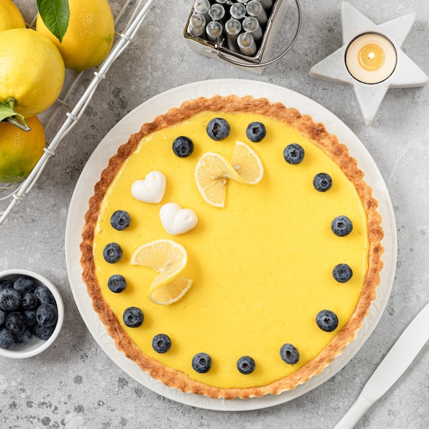 Traditional French lemon pie with blueberries on a white stone background