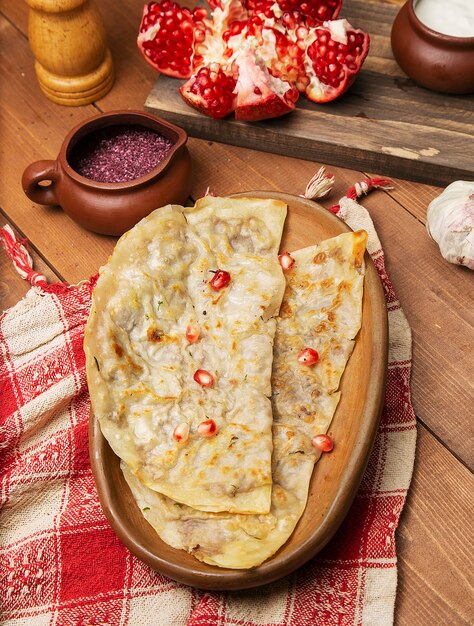 Traditional meat vegetable gutab, qutab, gozleme on wooden board with sumakh and pomegranate seeds