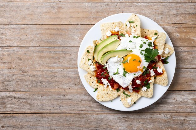 Traditional Mexican breakfast red chilaquiles with egg on wooden table