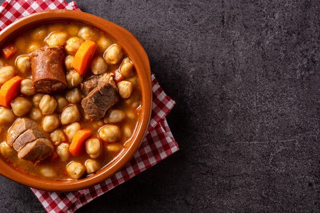 Traditional Spanish cocido madrileo in bowl on black background