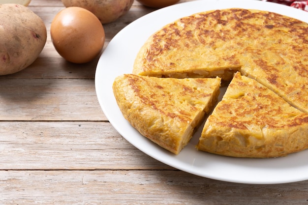 Foto gratuita omelette tradizionale spagnola con ingredienti su tavolo di legno