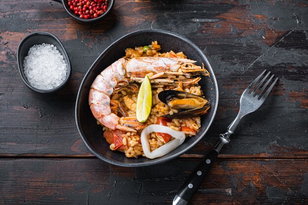 오래된 어두운 나무 테이블에 있는 검은 그릇에 해산물과 닭고기를 넣은 전통적인 스페인 빠에야, 꼭대기 전망, 음식 사진.