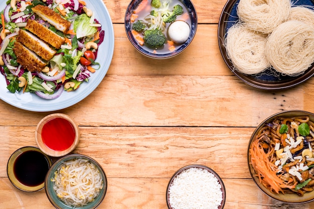 Traditional thai food including soup vegetables fried fish salad and rice vermicelli on wooden table