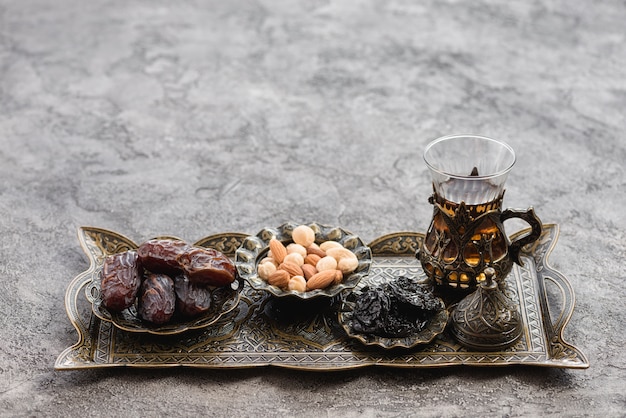 Traditional turkish arabic tea glasses; dates and nuts on metallic tray over the concrete backdrop