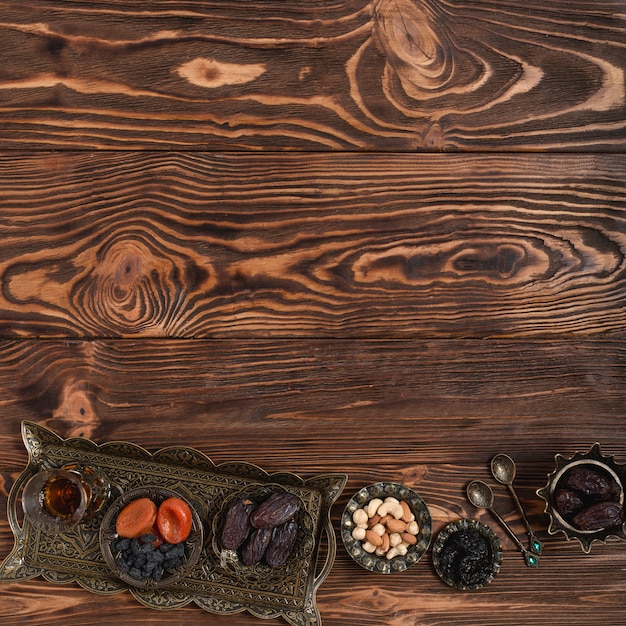 Traditional turkish metallic tray with tea glass; dried fruits and nuts on textured wooden backdrop with space for writing the text