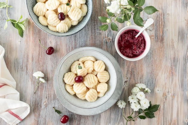 Traditional Ukrainian lazy cottage cheese dumplings served with sour cream and cherry sauce and fresh cherries on a wooden background