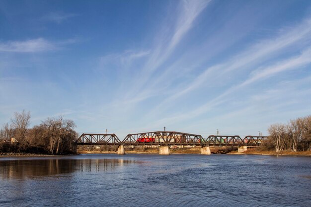 Train crossing a bridge over a body of water with blue skies and soft clouds in the background