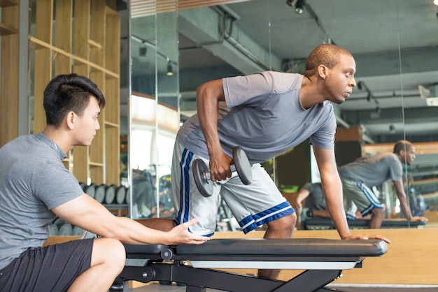 Trainer helping man lifting dumbbell in gym