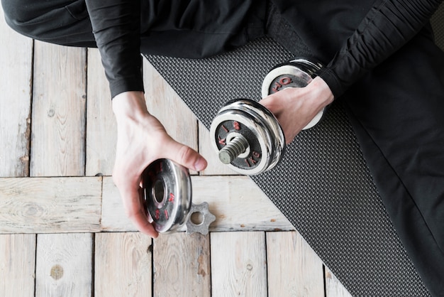 Free photo trainer sitting on floor and preparing dumbbell