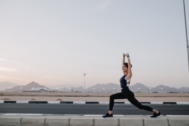 Training time, stretching on road in tropical country of joyful beautiful woman in sunny morning. Workout of strong sportswoman, energy, motivation, healthy lifestyle..