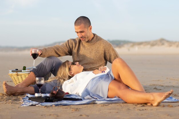 日没時のピクニックで静かなカップル。夕日の光線で毛布の上に座って横たわっているカジュアルな服装の男性と女性の上面図。ピクニック、食事、愛の概念