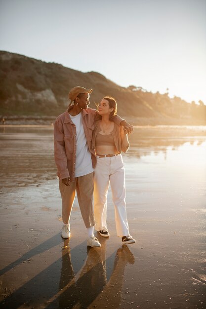お互いを保持し、日没時にビーチを歩くトランスのカップル