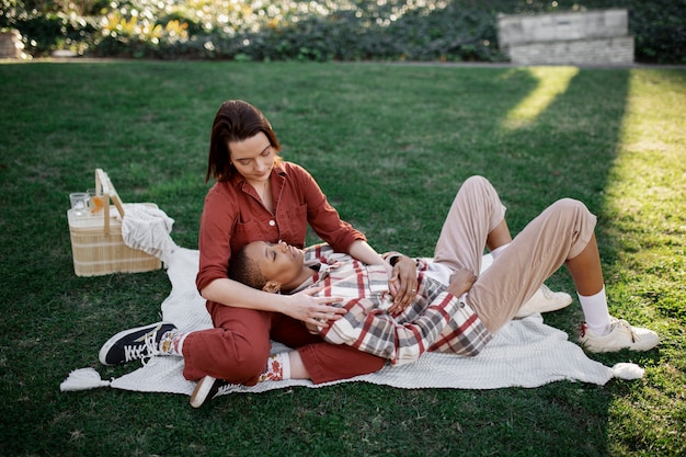 Foto gratuita uomo trans che tiene la testa sulle ginocchia della sua ragazza mentre fa un picnic al parco