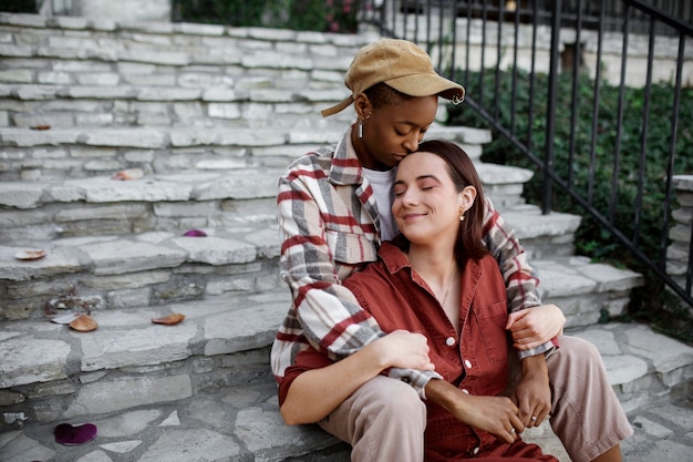 Free photo trans man kissing his girlfriend on the forehead while sitting on stairs